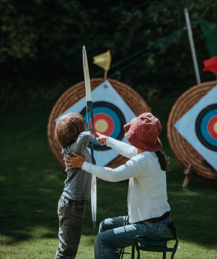 Kind mit Trainerin, welches mit Bogen auf Zielscheibe schießt