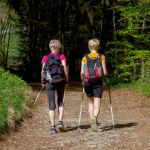 Zwei Frauen mit Nordic-Walking-Stöcken durch Wald laufend