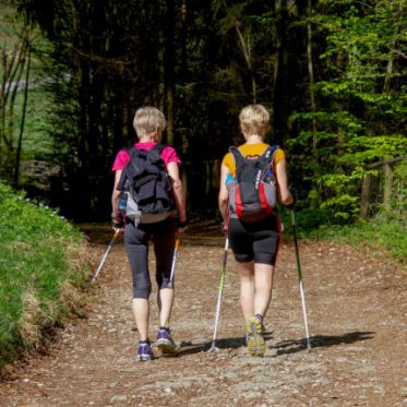Zwei Frauen mit Nordic-Walking-Stöcken durch Wald laufend