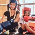 Trainerin mit Kind in Kickboxmontur im Ring sitzend