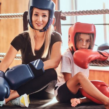 Trainerin mit Kind in Kickboxmontur im Ring sitzend