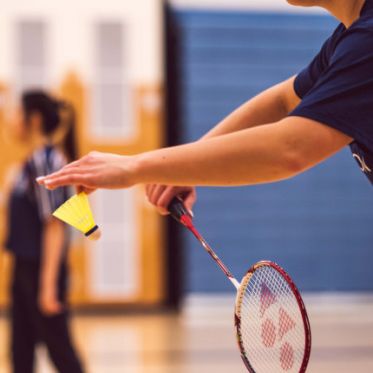 Mensch in Seitenansicht dabei einen Aufschlag im Badminton zu schlagen